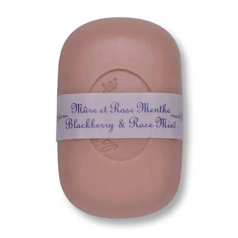 A bar of oval-shaped triple-milled soap with a light pink hue, wrapped in a decorative lavender band labeled "La Lavande Curved Bar Soap - Blackberry Rose Mint - 100gm.