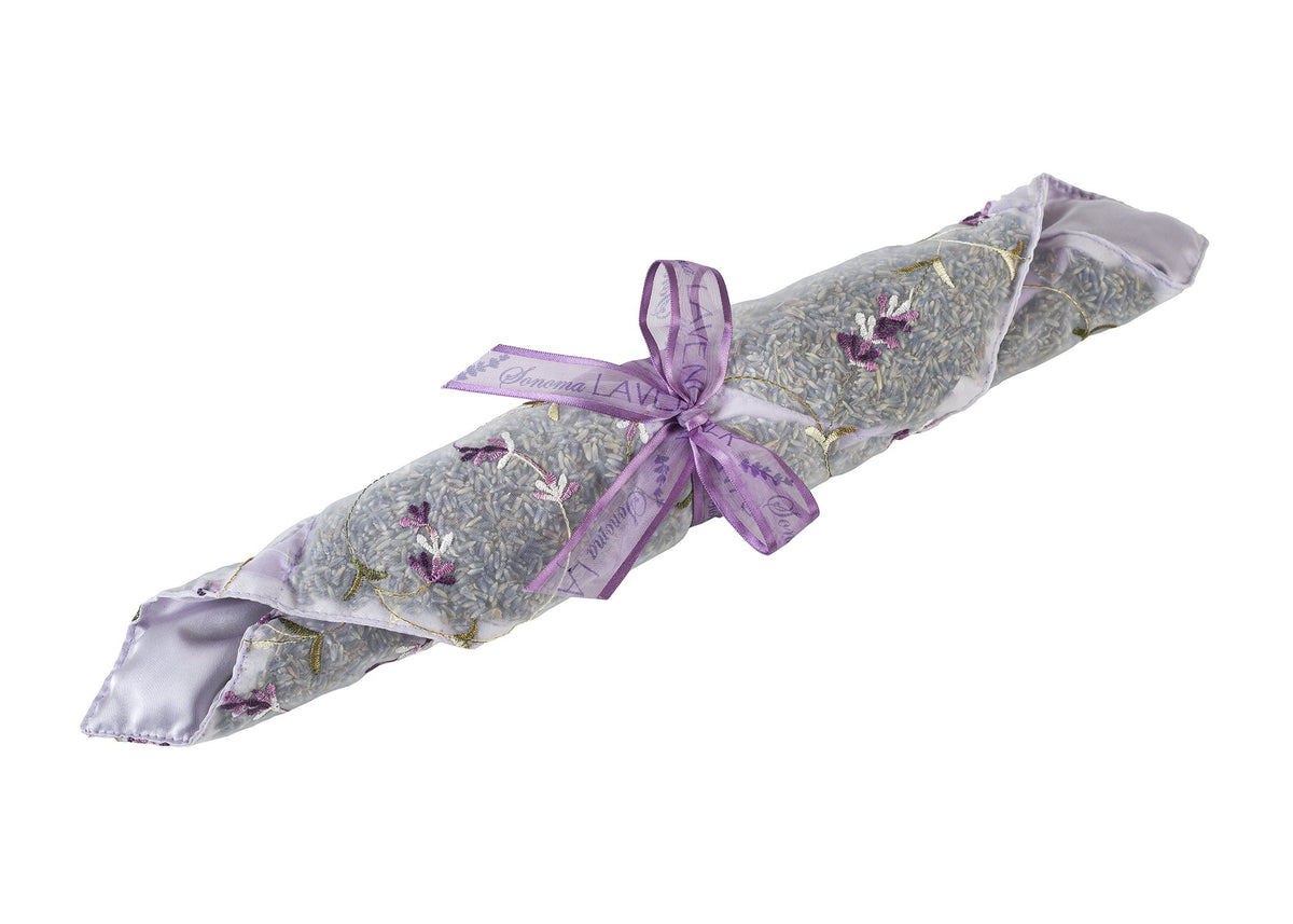 A Sonoma Lavender Liner wrapped in embroidered lavender fabric with delicate purple flowers visible inside, tied with a satin purple ribbon that has the word "lavender" printed on it.