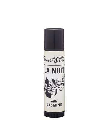 A cylindrical bottle labeled "Stewart & Claire - La Nuit Lip Balm" with "with jasmine and bergamot" beneath, featuring black and white floral designs, on a white background.