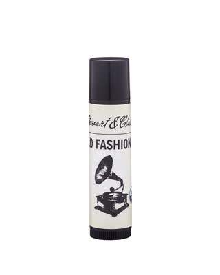 A tube of "Stewart & Claire Old Fashioned Lip Balm" lip balm featuring a vintage black telephone design on a white background with a black cap, made from recycled plastic.