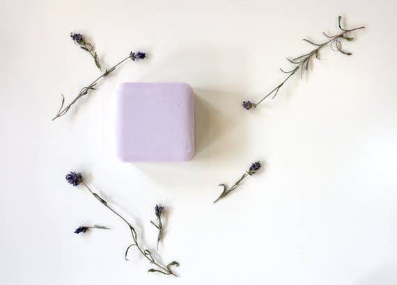 A Homegrown {77833} Co lavender bath bar centered on a plain white background, surrounded by scattered sprigs of lavender and small purple flowers.