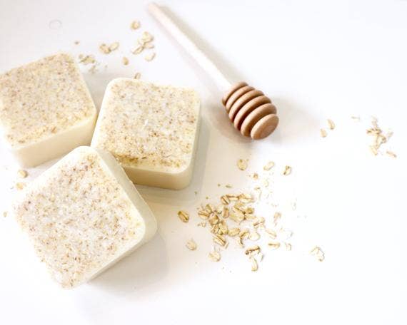 Three square Homegrown {77833} Co - Bi*** Better Have My Honey oatmeal milk honey soap bars beside a honey dipper, with oat flakes scattered on a white background.