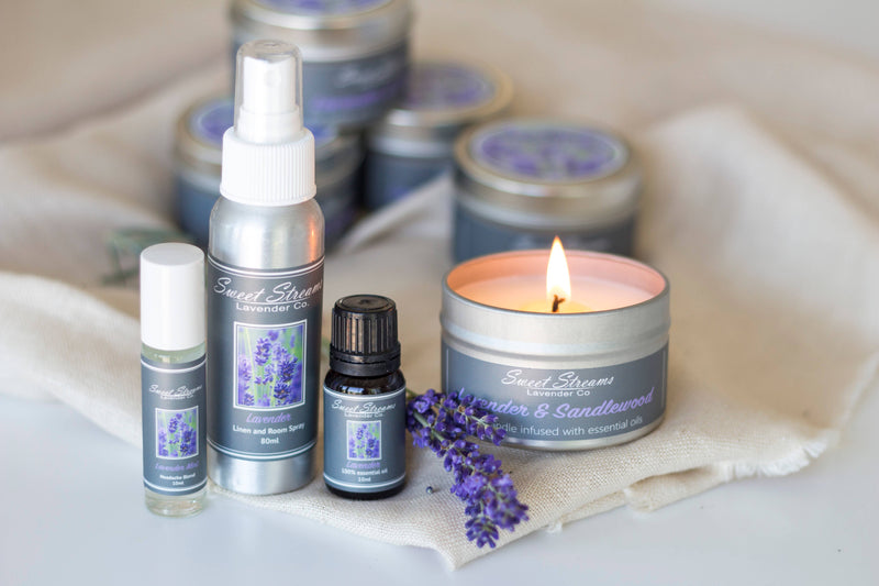 A collection of Sweet Streams Lavender Co. - Lavender Essentials Gift Sets including candles, a Lavender Linen Spray, and essential oils, arranged elegantly on a soft cloth with fresh lavender sprigs.