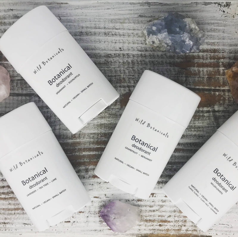 Four sticks of Wild Botanicals - Charcoal Lavender Deodorant on a wooden surface with scattered crystal pieces around them.