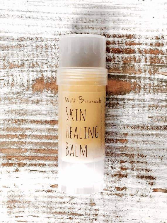 A container of Wild Botanicals Skin Healing Balm for dry skin rests on a rustic, white wooden surface with traces of beige paint.