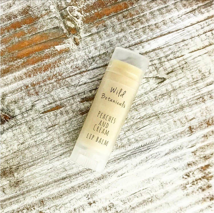 A tube of Wild Botanicals - Peaches and Cream Lip Balm lies on a weathered wooden surface.