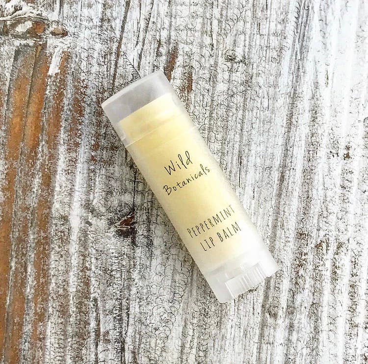 A tube of Wild Botanicals - Peppermint Lip Balm rests on a weathered wooden surface, highlighting the natural, simplistic design of the product packaging.