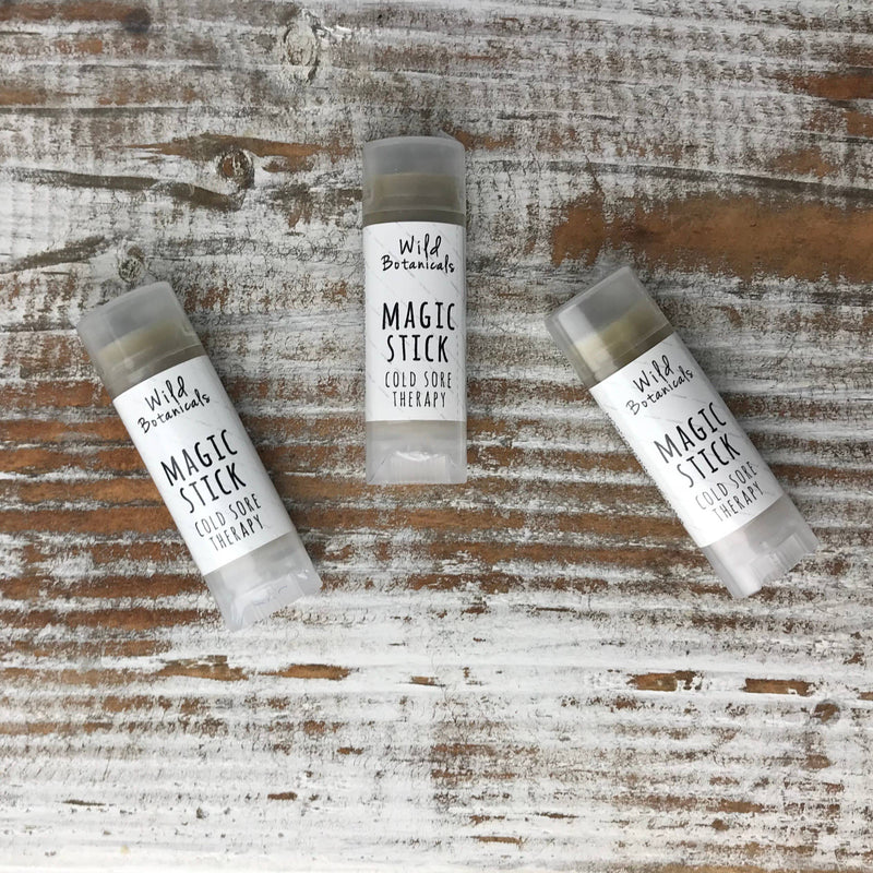 Four tubes of Wild Botanicals - Magic Stick Cold Sore Therapy Balm containing essential oils, laid on a rustic wooden surface.