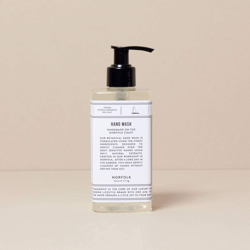 A bottle of Norfolk Natural Living Coastal hand wash with pump dispenser on a beige background. The label is white with minimalist design and text detailing the product's features.
