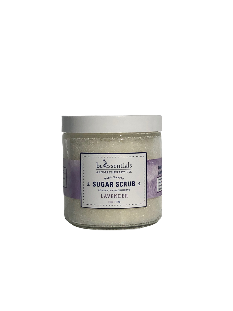 A jar of BC Essentials lavender sugar scrub - 16 oz, against a solid gray background. The jar is clear with a silver cap, displaying the light purple scrub.
