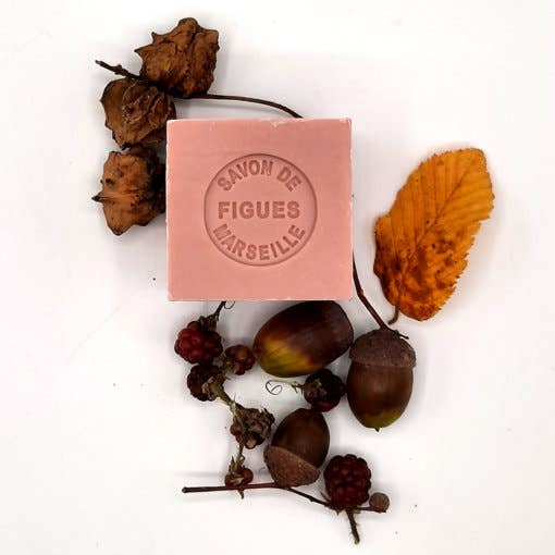 A bar of French soap labeled "Senteurs De France Marseille Fig Cube Soap" surrounded by autumn leaves, acorns, and berries on a white background.