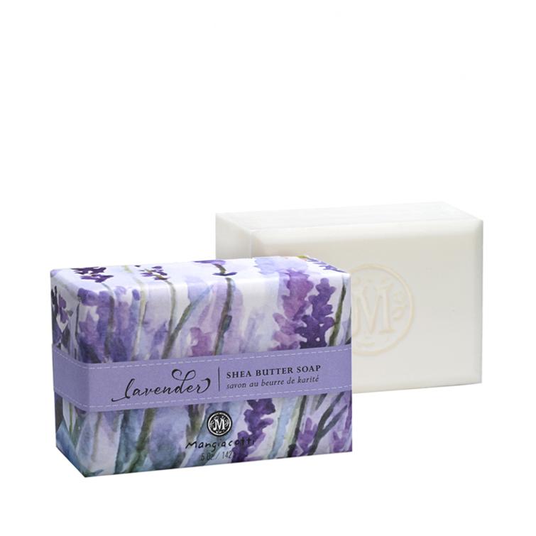 A bar of Mangiacotti Lavender Shea Butter Bar Soap wrapped in lavender-themed packaging with the word "lavender" and the soap itself next to the box, showing an embossed logo. This triple-milled body bar by Mangiacotti.