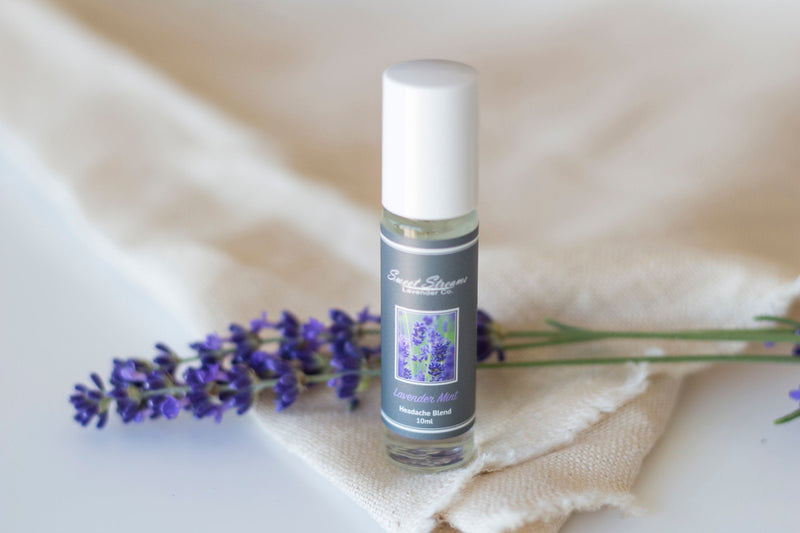 A bottle of Sweet Streams Lavender Co. - Lavender Mint Eucalyptus Breathe Blend Roller with a fresh lavender sprig beside it, displayed on a beige cloth against a white background.