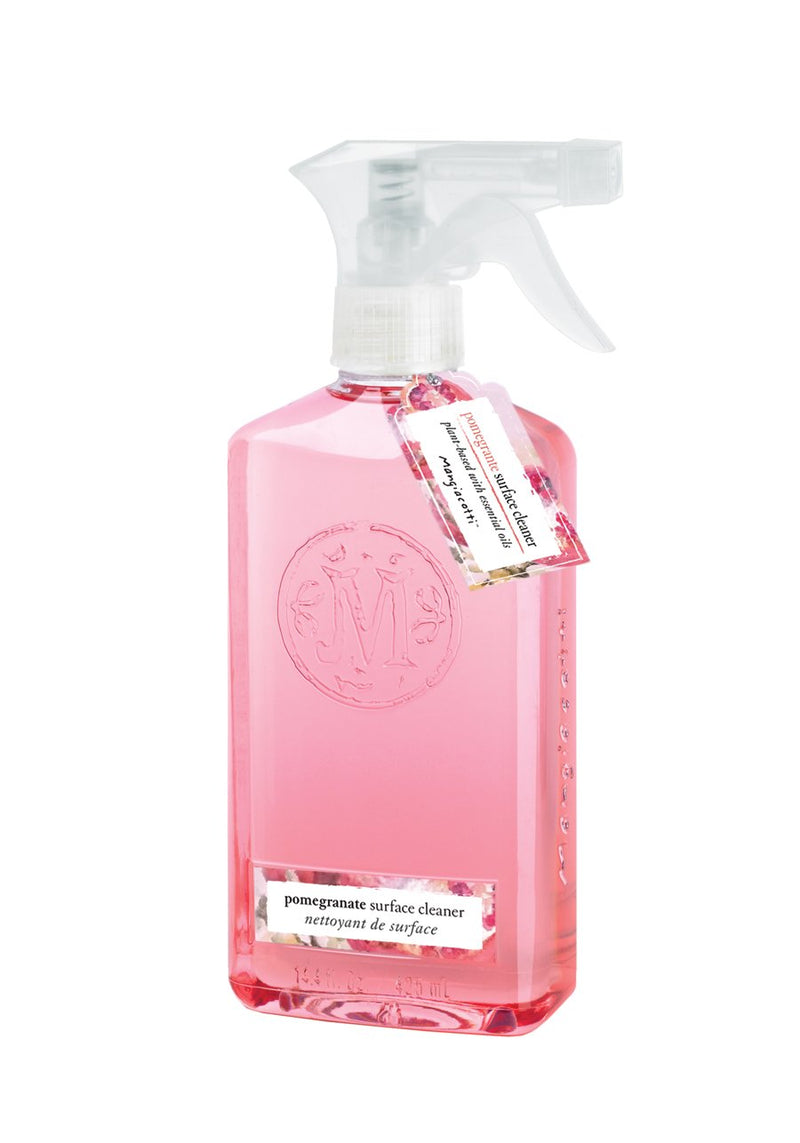 A transparent spray bottle of pink Mangiacotti Pomegranate Surface Cleaner with a label and white text detailing the brand and product type. The cleaner is visible through the container.