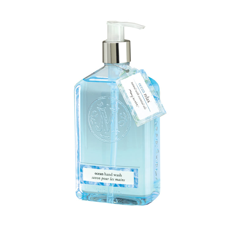 A clear bottle of Mangiacotti Ocean Natural Hand Wash with a pump dispenser. The blue, plant-based liquid inside is visible, and a label hangs from the neck of the bottle, featuring product details.