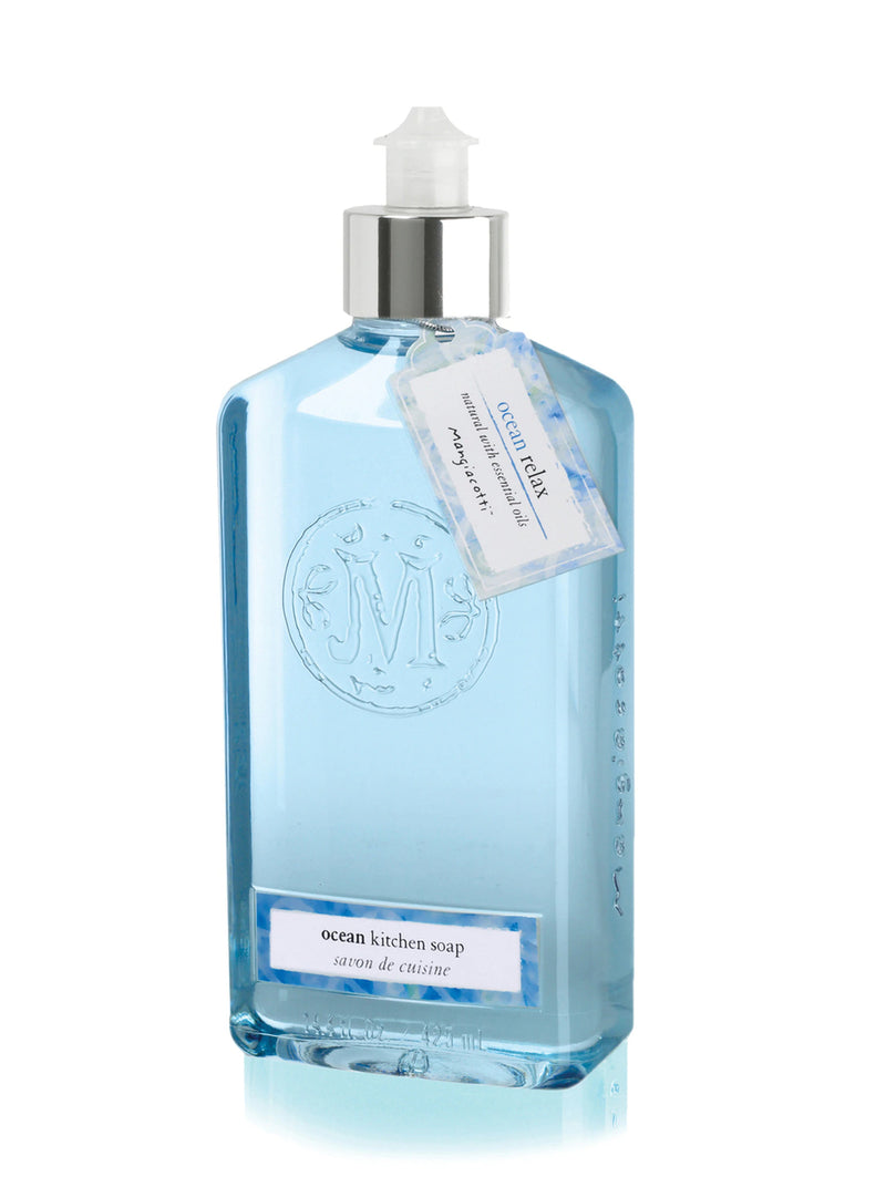 A clear glass bottle of blue liquid soap labeled "Mangiacotti Ocean Natural Kitchen Soap" with a silver pump dispenser. The bottle has embossed decorations and a hanging tag with text.