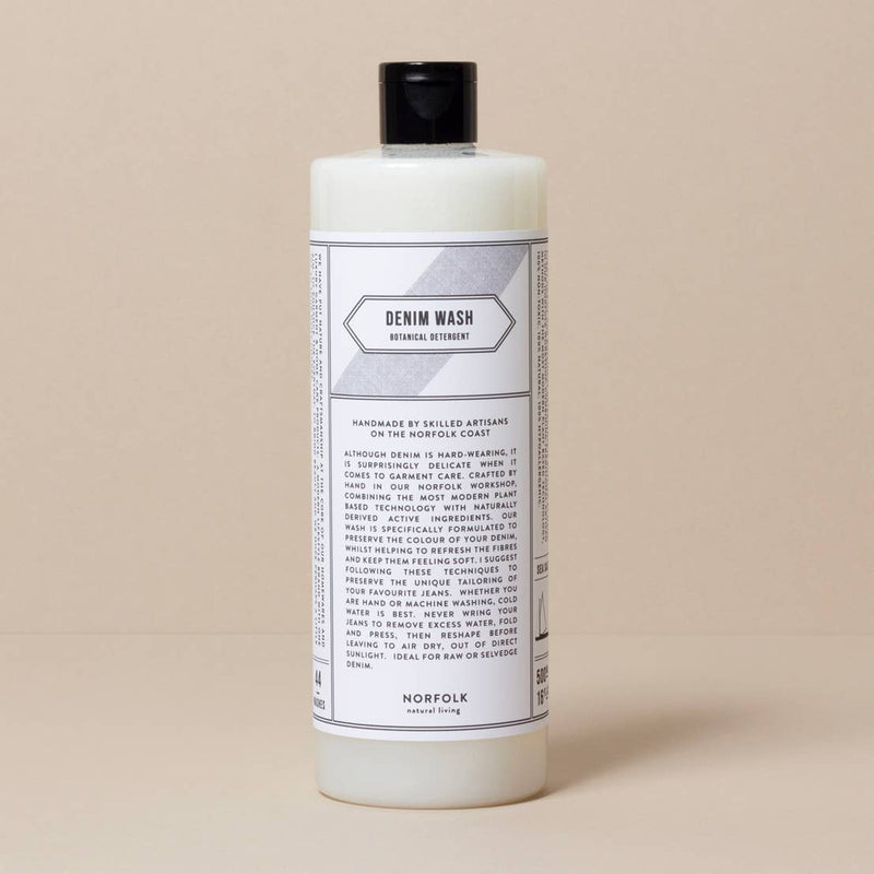 A bottle of "Norfolk Natural Living Coastal Denim Wash - 500ml" laundry detergent with detailed usage instructions and branding labels on a plain, beige background.