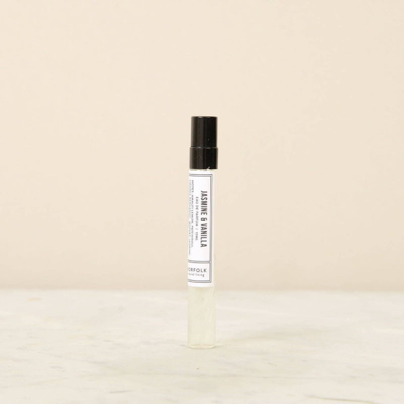 A clear glass roller bottle of Norfolk Natural Living - Jasmine & Vanilla Parfum 10ml displayed on a marble surface with a beige background, labeled in a simple, modern font.