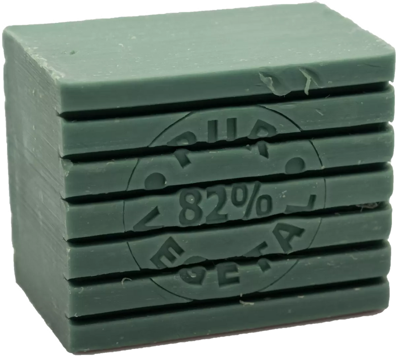 A stack of La Savonnerie de Nyons Striped Soap -Olive 300gm bars with embossed Cyrillic text and the number 82%, all set against a plain light background. The top bar shows slight chipping on its edge and contains organic shea.