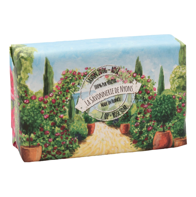 A colorful La Savonnerie de Nyons soap box with a picturesque illustration of a garden pathway lined by trees and rose bushes, labeled "Rose scented soap, La Savonnerie de Nyons Jardin de Roses made in France.