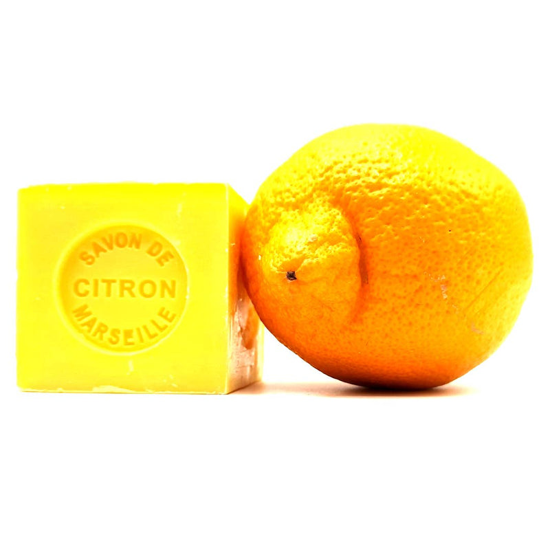 A vibrant yellow Senteurs De France Marseille Lemon Cube soap labeled "savon de citron" next to a fresh orange on a plain white background.