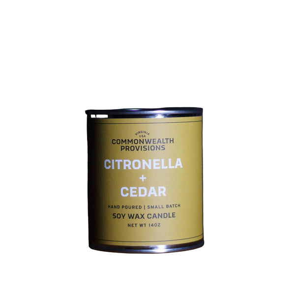 A golden yellow Commonwealth Provisions Citronella + Cedar Candle in a small tin labeled "commonwealth provisions" on a dark background with soft lighting.