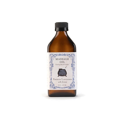 A brown glass bottle labeled "Three Sisters Apothecary French Lavender Massage Oil" with the text "steam-distilled lavender with arnica" stands against a plain white background.