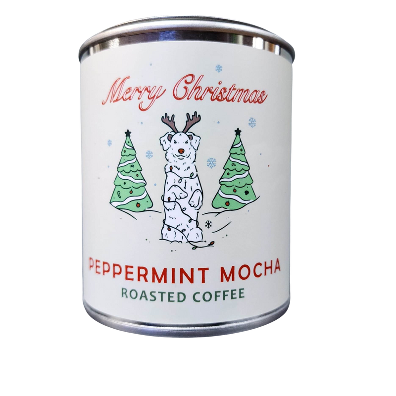 A festive holiday-themed coffee tin labeled "Fox + Hound Christmas Peppermint Mocha Flavored Coffee" featuring a cheerful snowman and green Christmas trees against a white background.