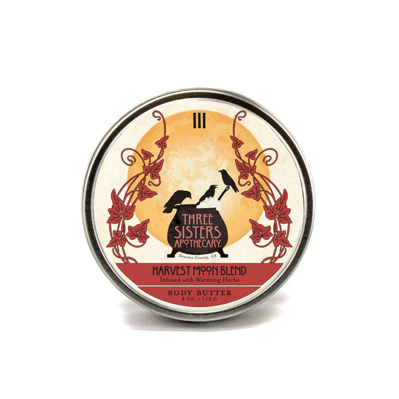 A round tin of Three Sisters Apothecary Harvest Moon Body Butter enriched with shea butter, featuring an ornate label with silhouettes of flying birds and floral designs against a harvest moon backdrop.