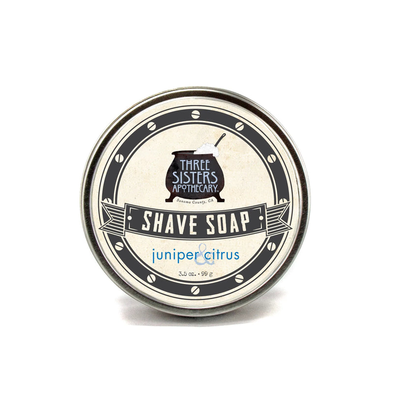 A closed tin of Three Sisters Apothecary Shave Soap - Juniper & Citrus labeled on a white background. The design features vintage-style black and white graphics.