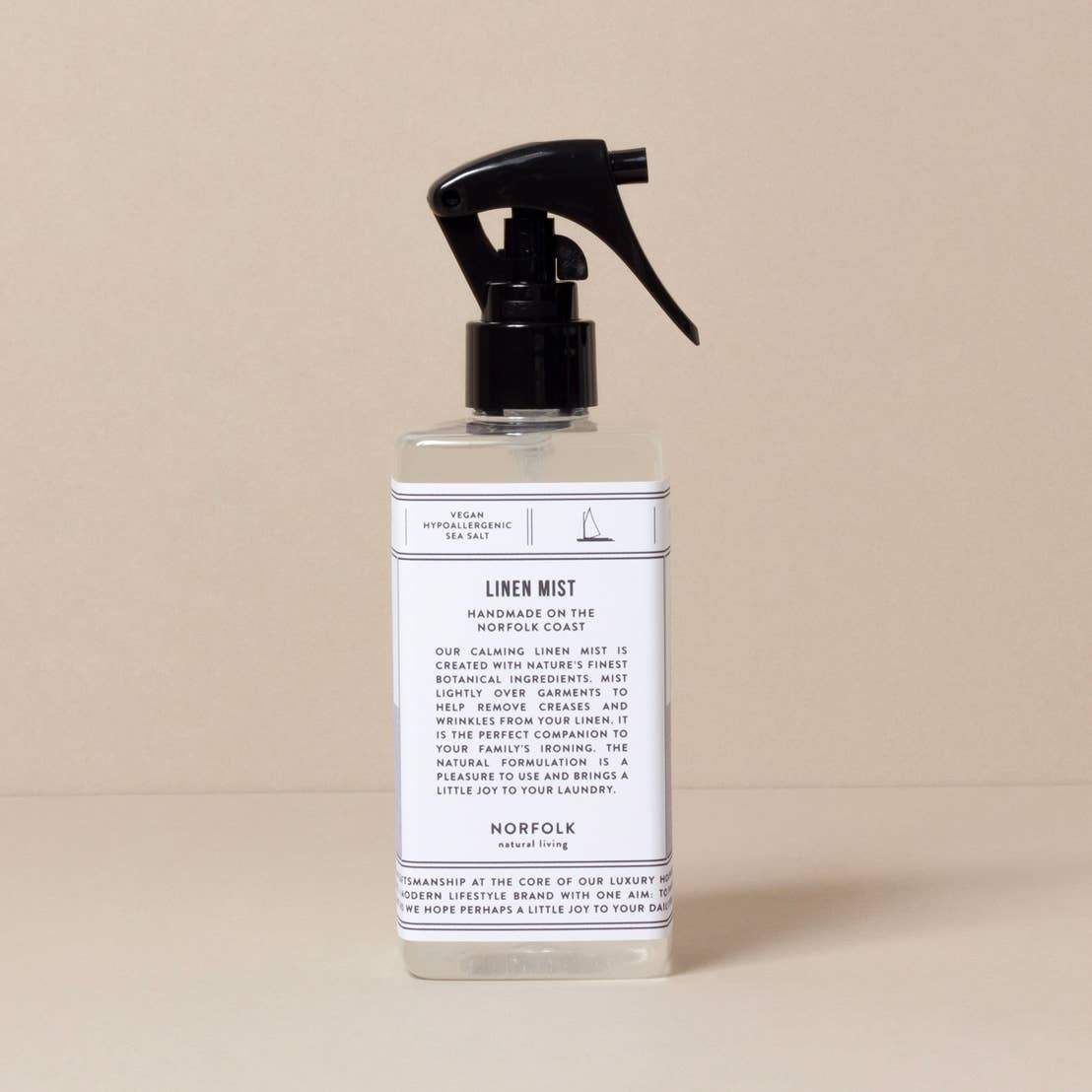 A bottle of Norfolk Natural Living Coastal Linen Mist room spray with a spray nozzle, labeled with details about its scent and ingredients, against a plain beige background.