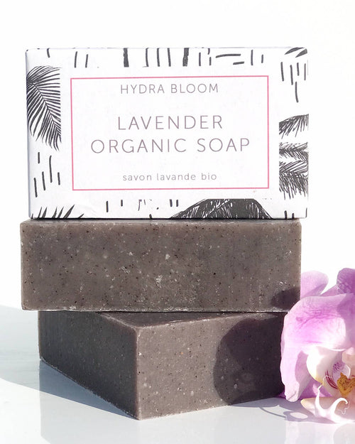 Two bars of Hydra Bloom Beauty Lavender organic hand soap stacked on top of each other next to a pink orchid, with a box labeled "Hydra Bloom Beauty Relax Lavender Organic Soap" in the background.