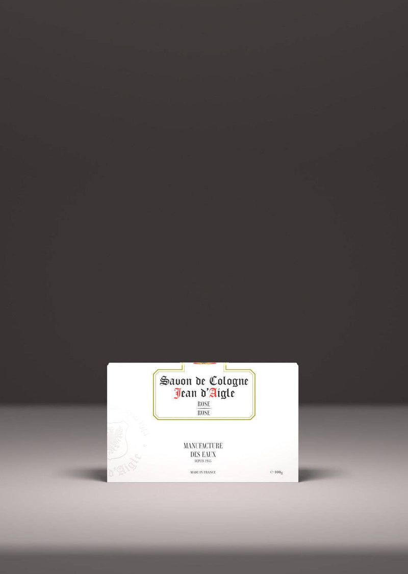 A vintage-style soap package, labeled "Jean d'Aigle Rose Soap" by Jean d'Aigle, highlighted by a spotlight, placed centrally against a grey background.