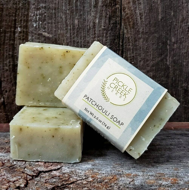 Three bars of Pickle Creek Herbs Patchouli Herbal Soap with labels on a wooden background.