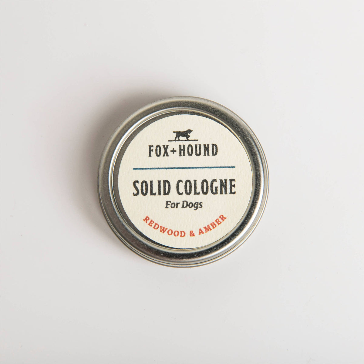 A closed tin of Fox + Hound Redwood and Amber Solid Dog Cologne, displayed on a white background.