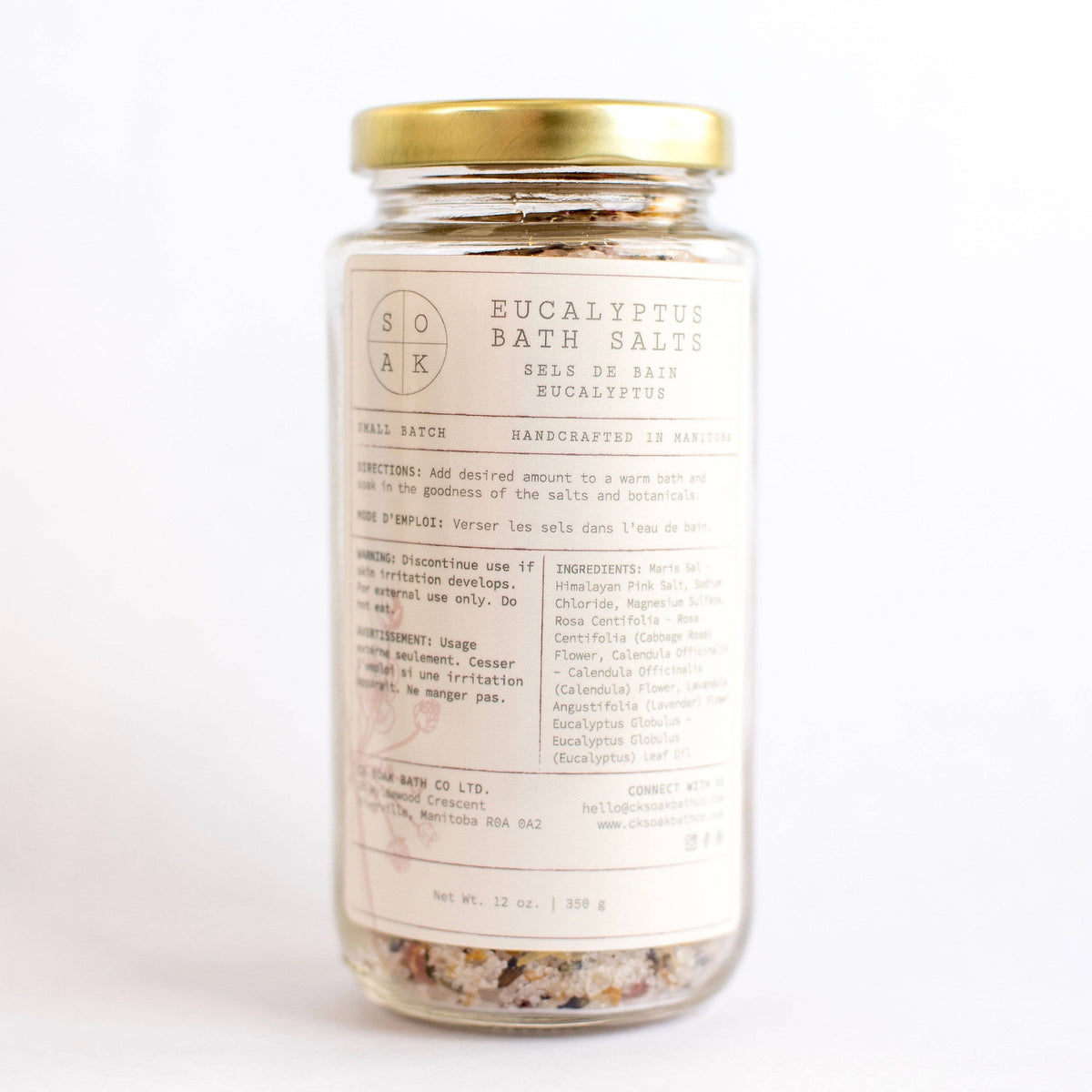 A clear glass jar filled with SOAK Bath Co.'s Eucalyptus Bath Salt blend labeled "eucalyptus bath salts", featuring ingredient details and branding. The background is bright and clean.