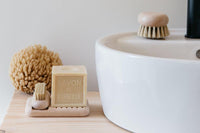 A bathroom sink with a bar of soap labeled "savon de marseille" on an Andrée Jardin Tradition Beech Wood Soap Holder, a scrub brush, and a natural sponge arranged neatly beside the basin.