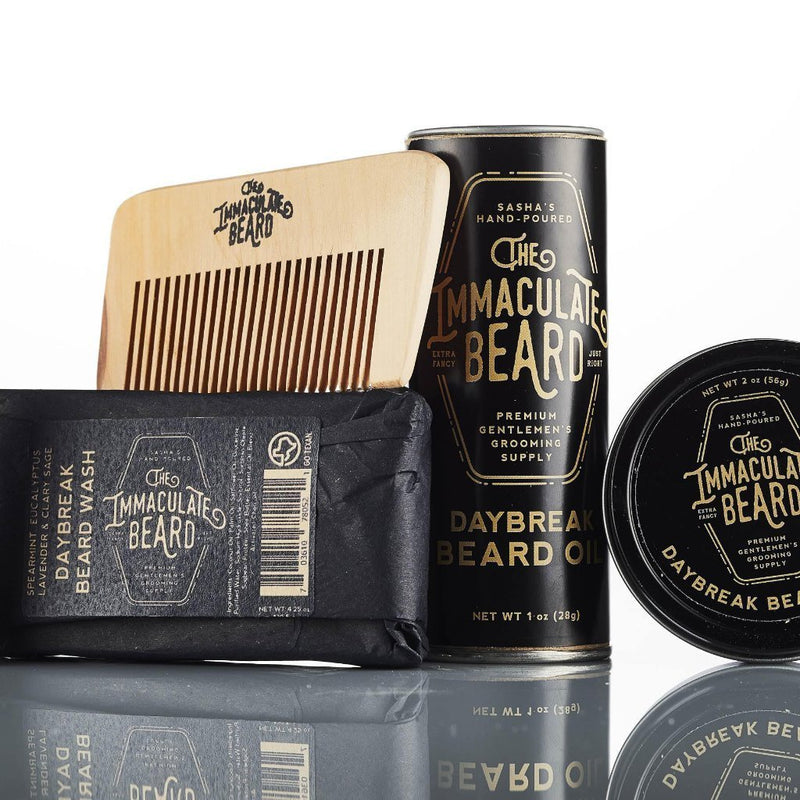 A The Immaculate Beard beard grooming kit featuring products for beard care, including a wooden comb, a black tin of beard balm, a bottle of beard oil, and a black soap bar.