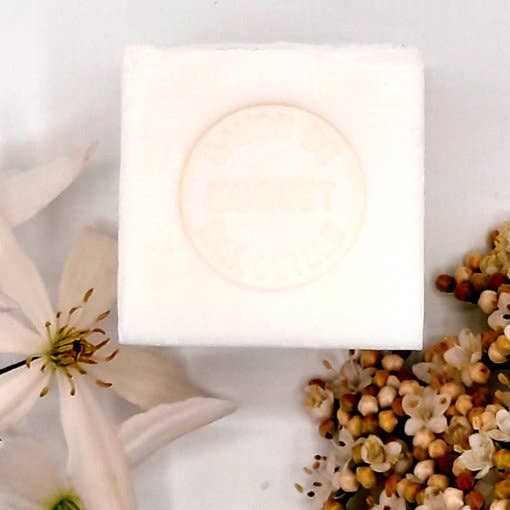 Senteurs De France Marseille Lily of the Valley Cube Soap with an embossed circle design, surrounded by white flowers and small dried buds on a light background.