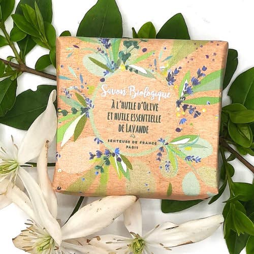 A square soap bar with a vintage floral print packaging, labeled "Senteurs De France Organic Lavender Essential Oil Soap", surrounded by green.