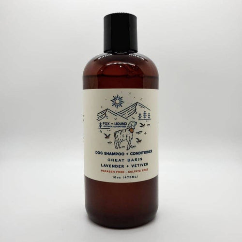A brown bottle of "Fox + Hound Great Basin Dog Shampoo + Conditioner National Park Series" by Fox + Hound, featuring a label with mountains, sun, and a dog on a plain white background.