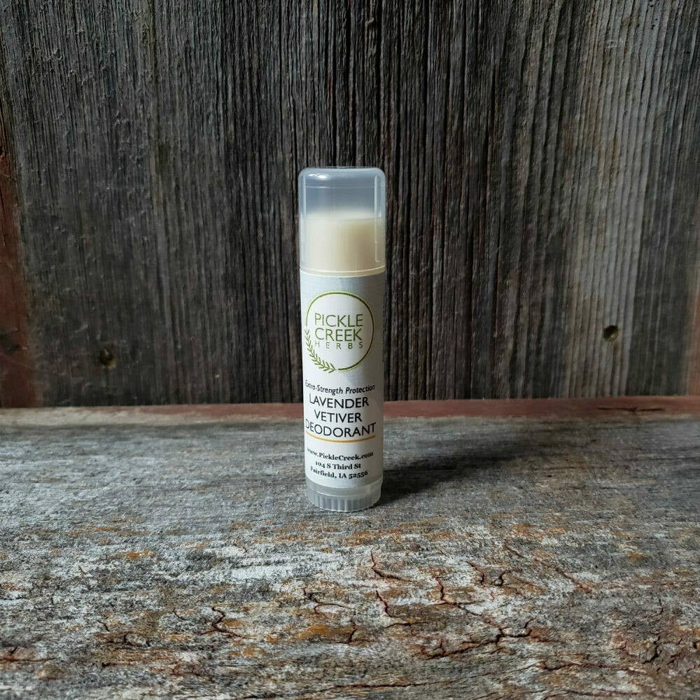 A stick of Pickle Creek Herbs Lavender Vetiver deodorant for extra-strength protection on a wooden surface against a rustic wooden backdrop.