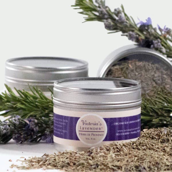 Two tins of Victoria's Lavender Herbs de Provence labeled "Victoria's Lavender" with sprigs of French lavender and dried lavender scattered around, on a white background.