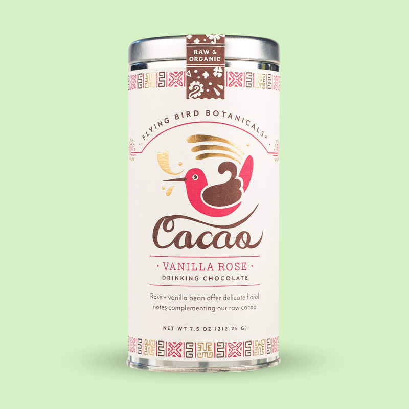 A canister of Flying Bird Botanicals' Vanilla Rose Cacao - Large Tin against a light green background. The label features a whimsical illustration of a bird holding an organic vanilla bean flower.