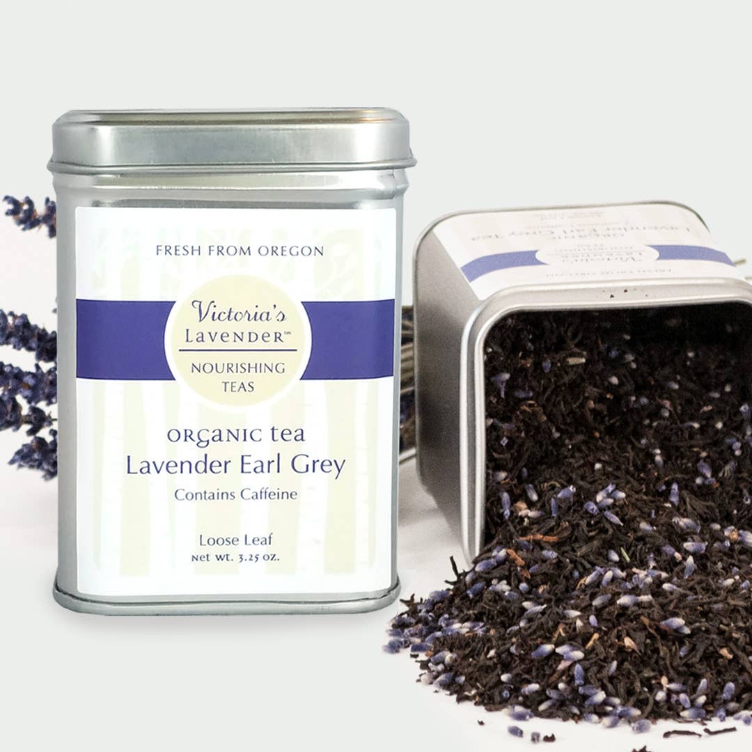 Two tins of Victoria's Lavender Organic Tea - Lavender Earl Grey, Loose Leaf, one upright showing the label and one tipped with loose leaves spilling out, against a neutral background with lavender sprigs.