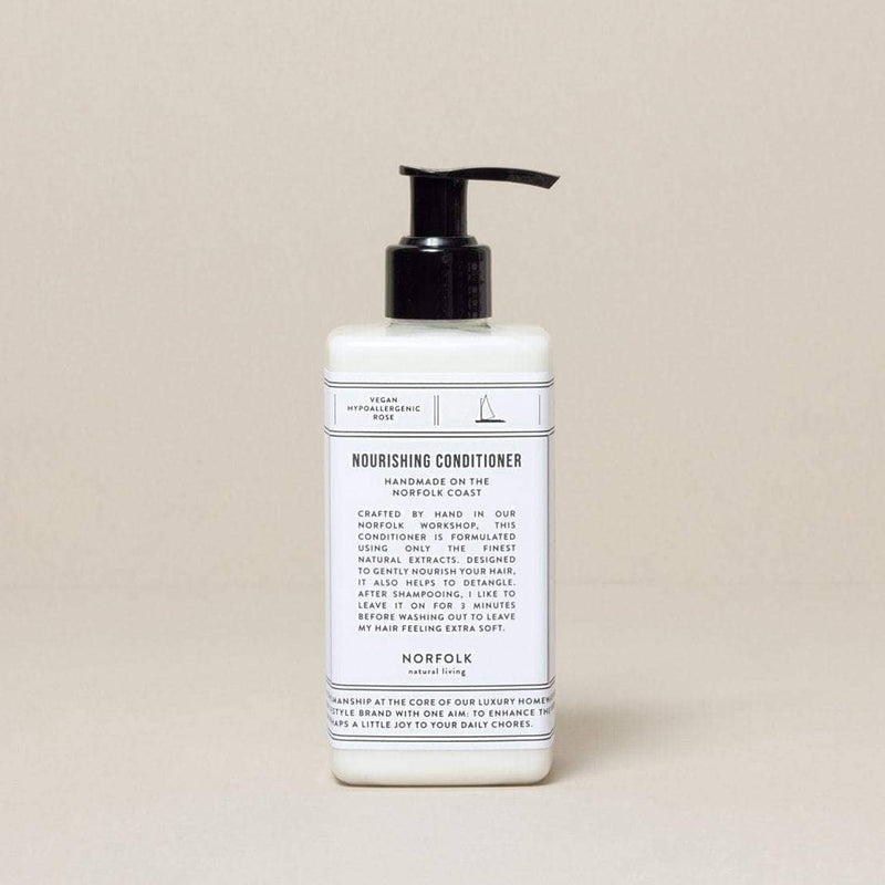 A bottle of Norfolk Natural Living Coastal Nourishing Conditioner 300ml with a pump dispenser against a neutral beige background. The label includes product details and benefits, featuring coconut oil.