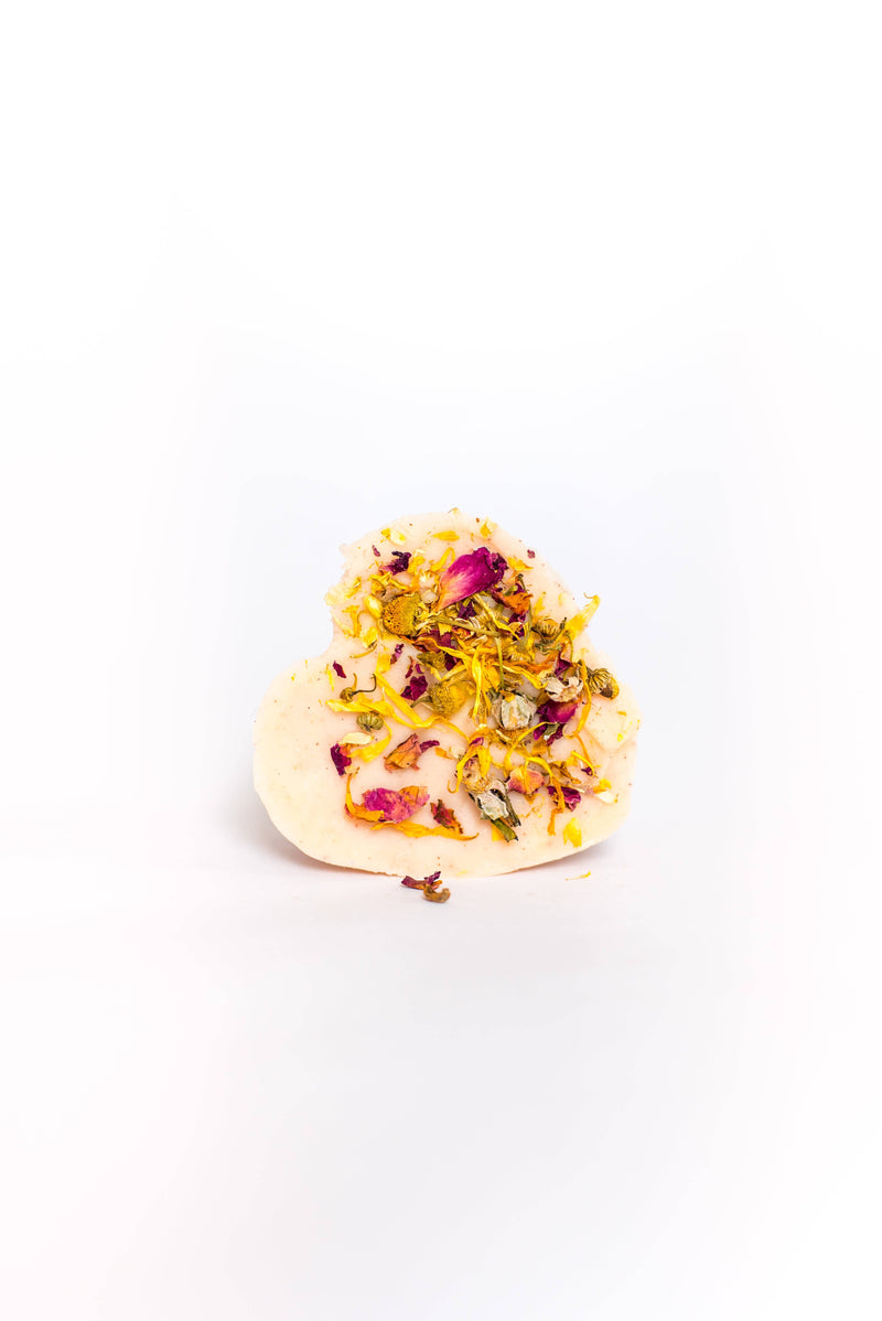 A SOAK Bath Co. heart-shaped soap adorned with dried flower petals on a white background. The soap's decoration is colorful, featuring shades of yellow, pink, and green, perfect as a gift for mom.