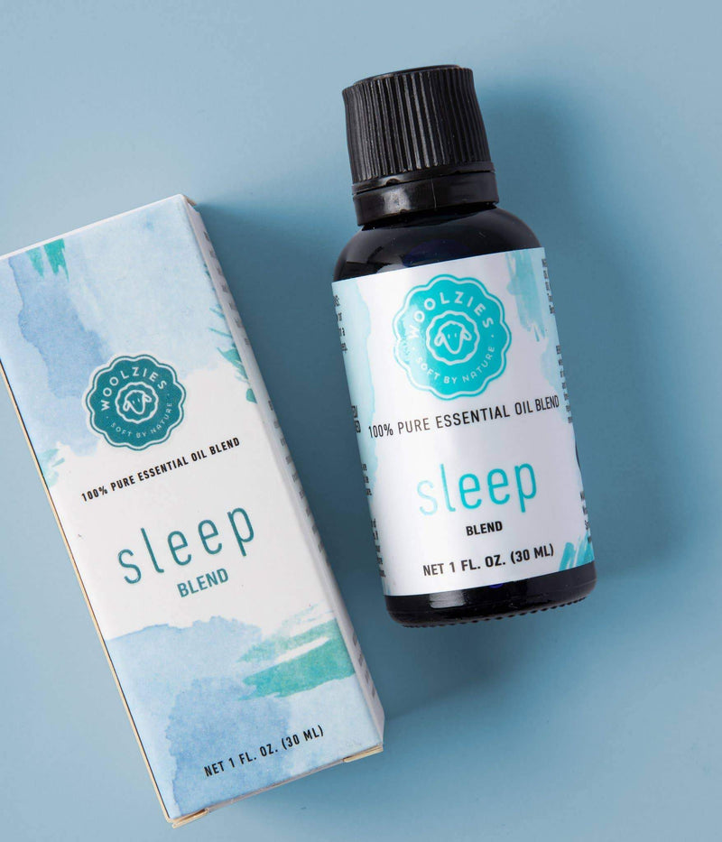 A bottle of Woolzies Good Night Sleep Blend Essential Oil next to its box, both labeled "100% pure essential oil blend for insomnia relief." The packaging features blue and white design elements, set against a light.