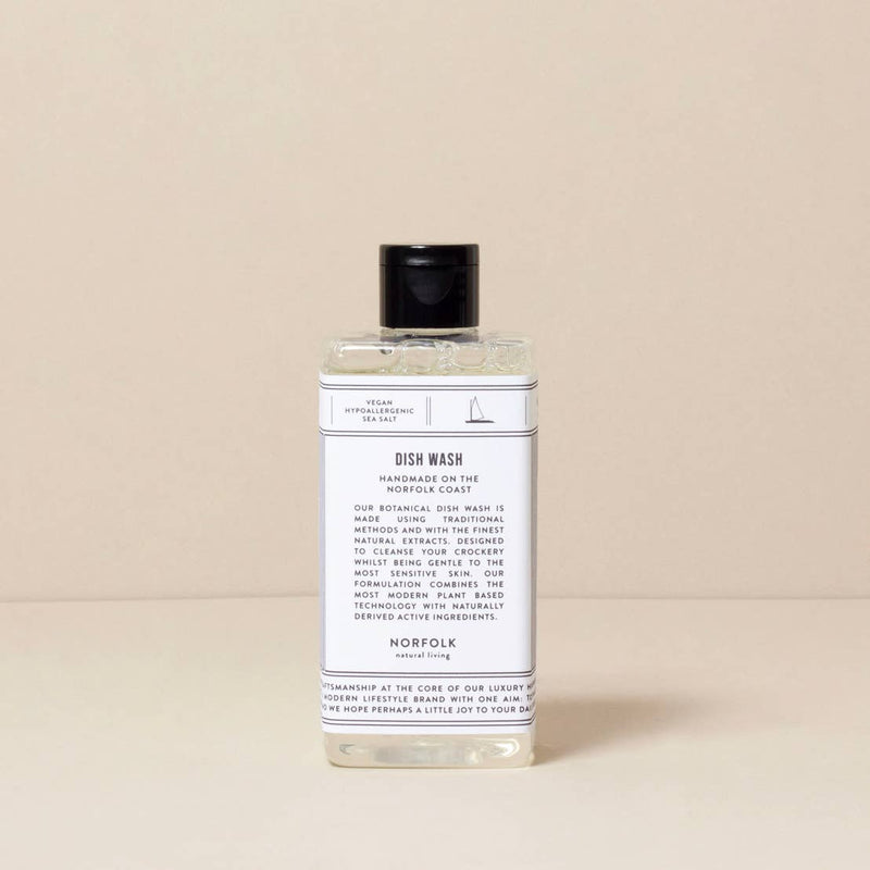 A clear bottle of Norfolk Natural Living Coastal Dish Wash -300ml with a black cap, labeled in elegant typography, against a light beige background.
