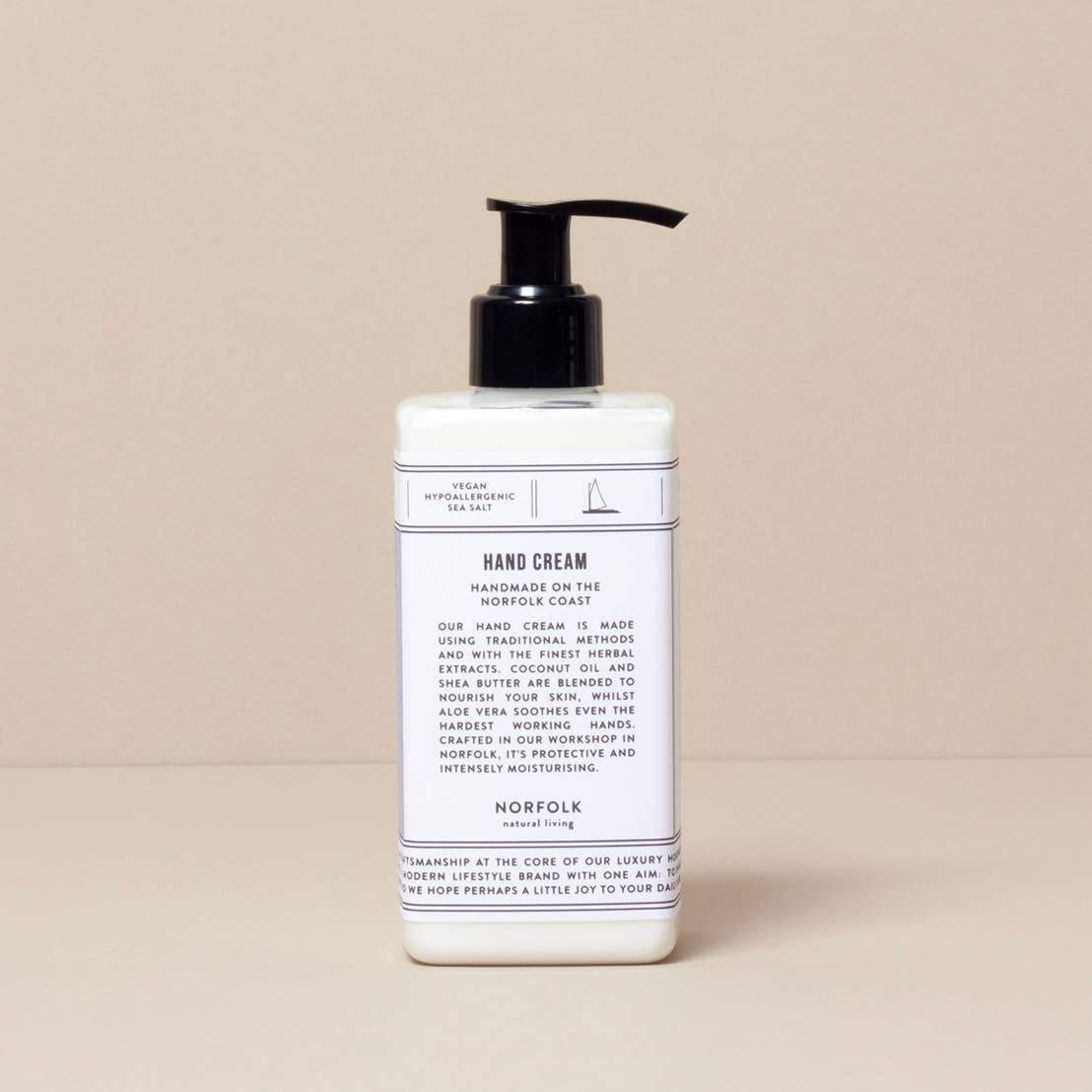 A bottle of Norfolk Natural Living Coastal Hand Lotion with a pump dispenser on a beige background. The label includes text describing the product's moisturizing features and origin.
